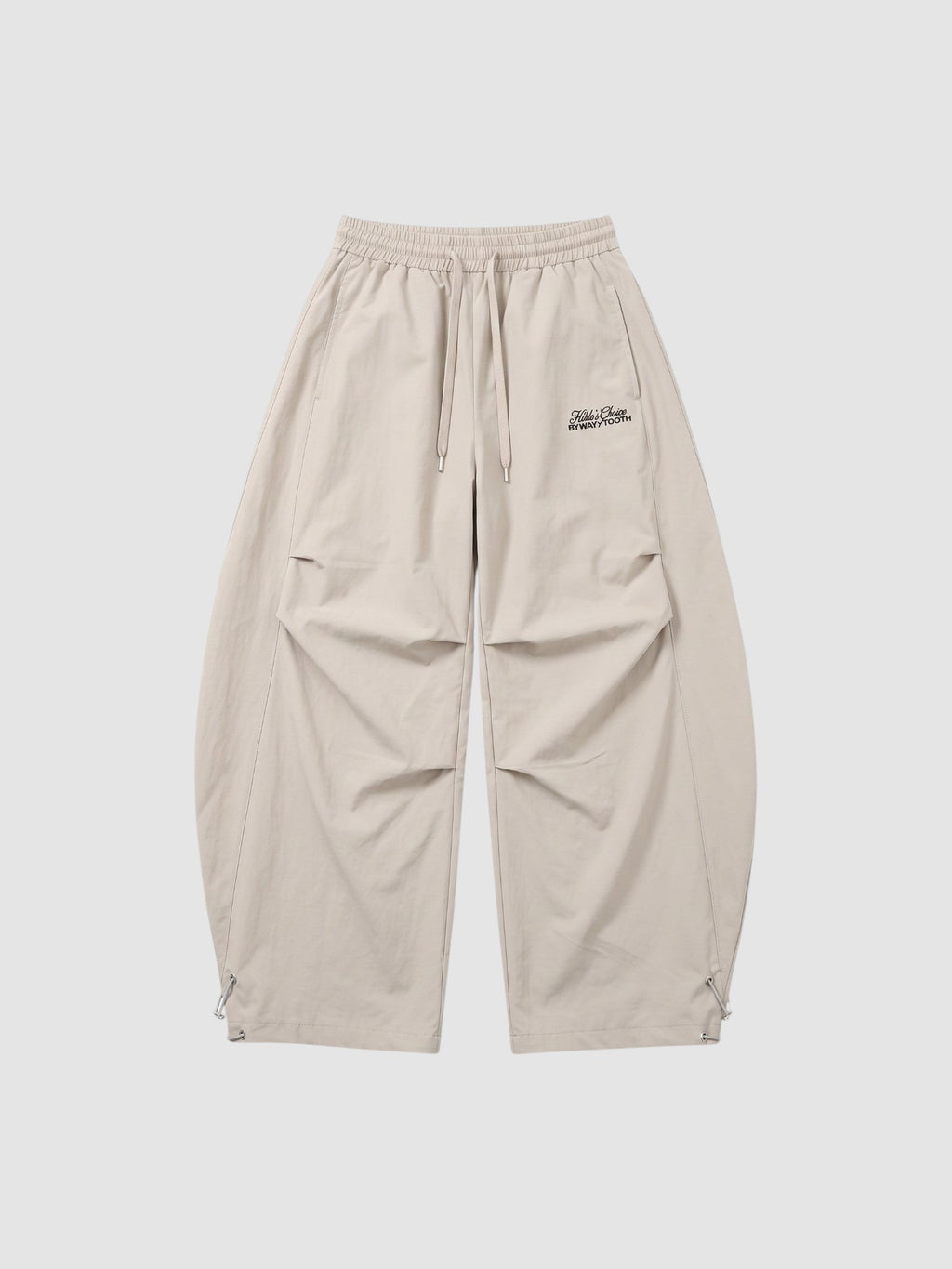 Y2K Studio beige oversized nylon joggers with elastic waist, side pockets, and white embroidered script logo on thigh.