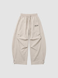 Y2K Studio beige oversized nylon joggers with elastic waist, side pockets, and white embroidered script logo on thigh.