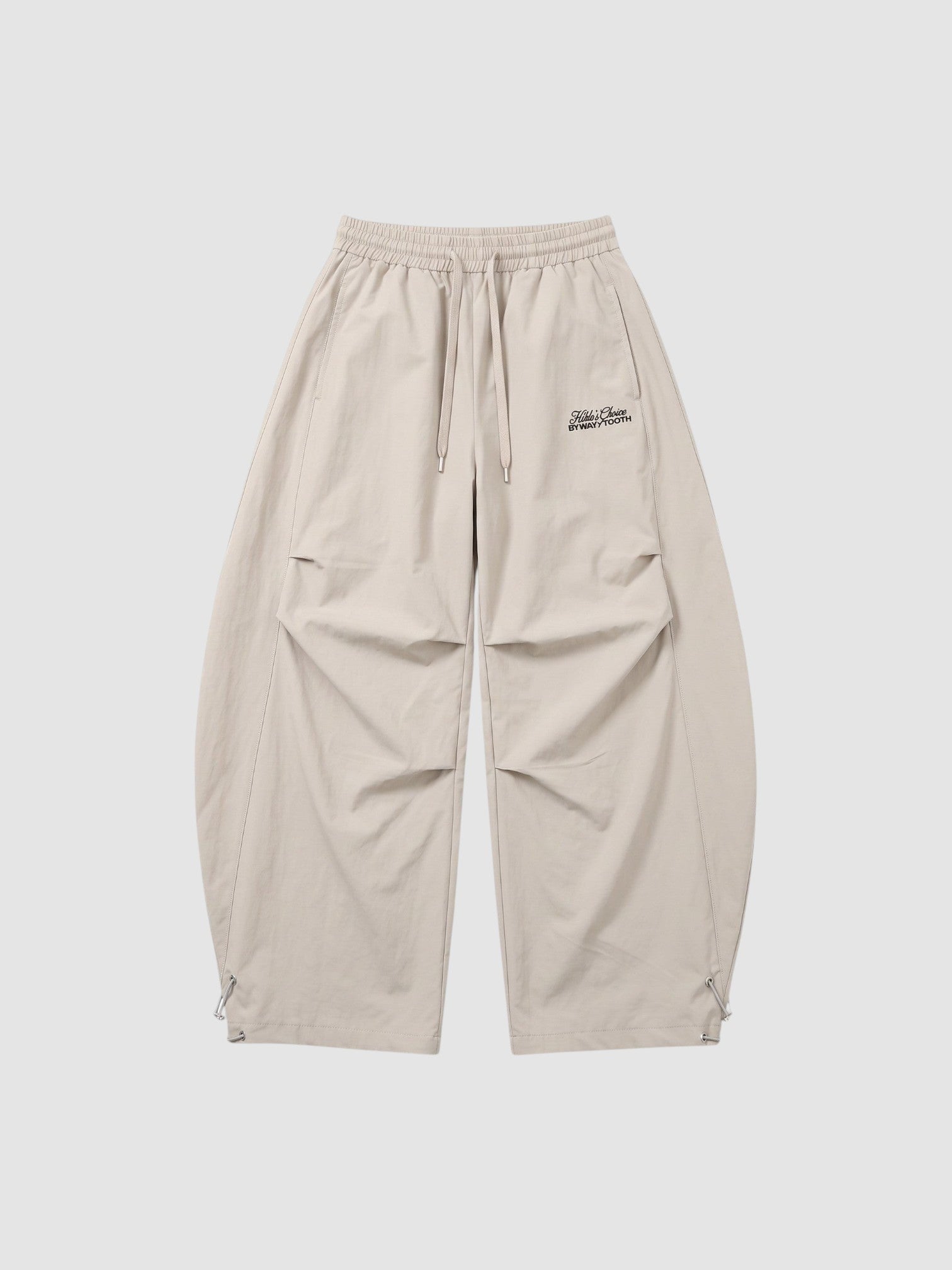 Y2K Studio beige oversized nylon joggers with elastic waist, side pockets, and white embroidered script logo on thigh.