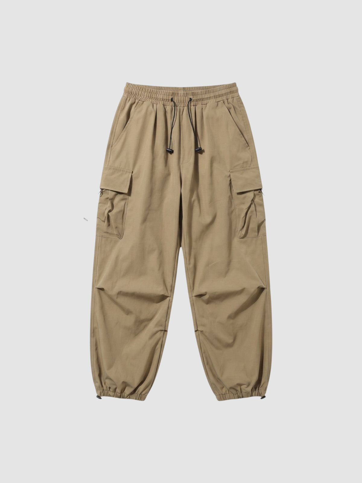 Y2K Studio beige parachute cargo pants with elastic waist, drawstring cuffs, and side flap pockets in matte fabric.