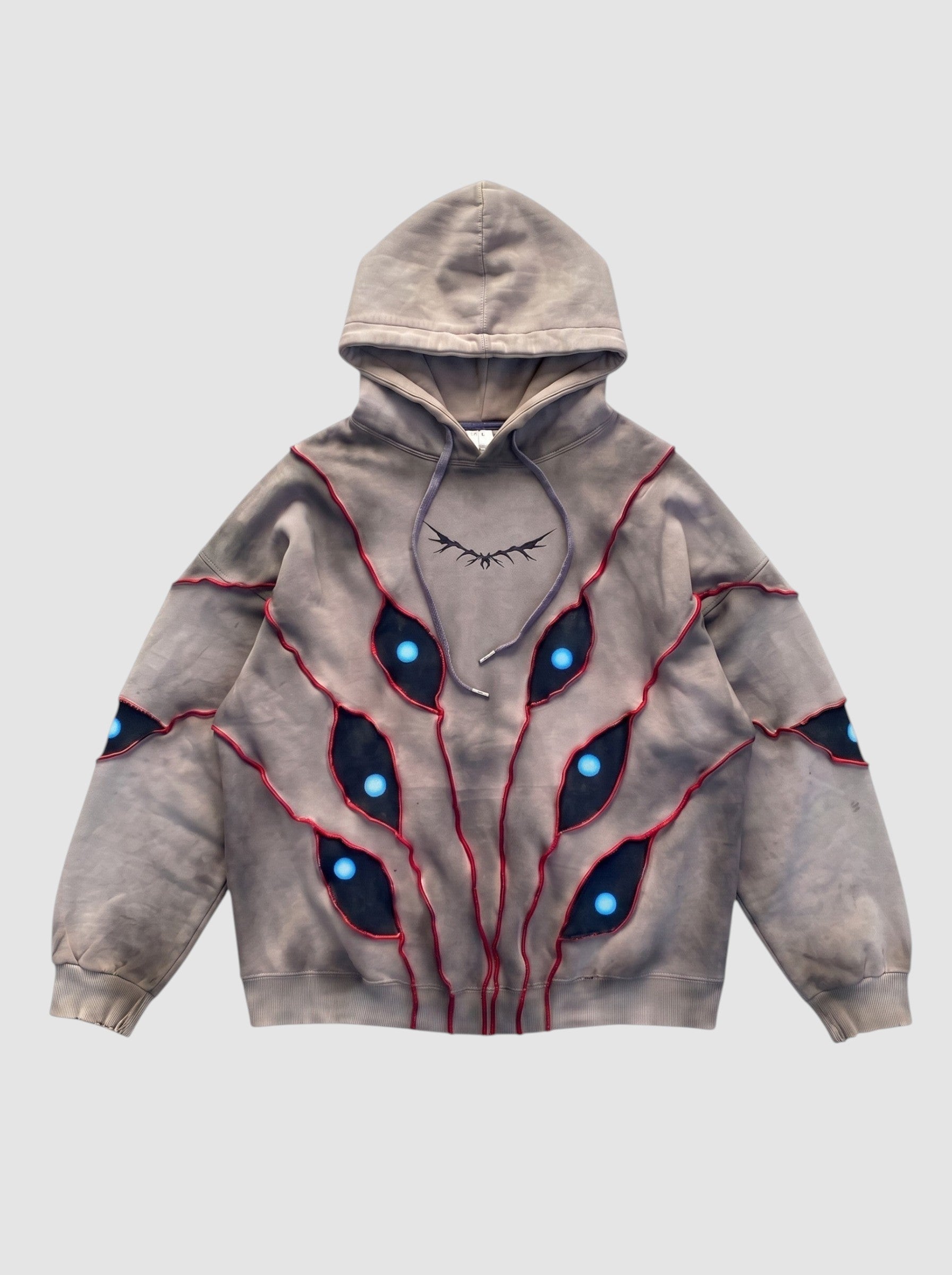 Y2K Studio oversized beige hoodie with patchwork eye cutouts, blue pupils, and red relief stitching details.