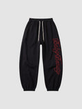 Y2K Studio black oversize joggers with red calligraphy lettering down the leg and a cream drawstring waist.