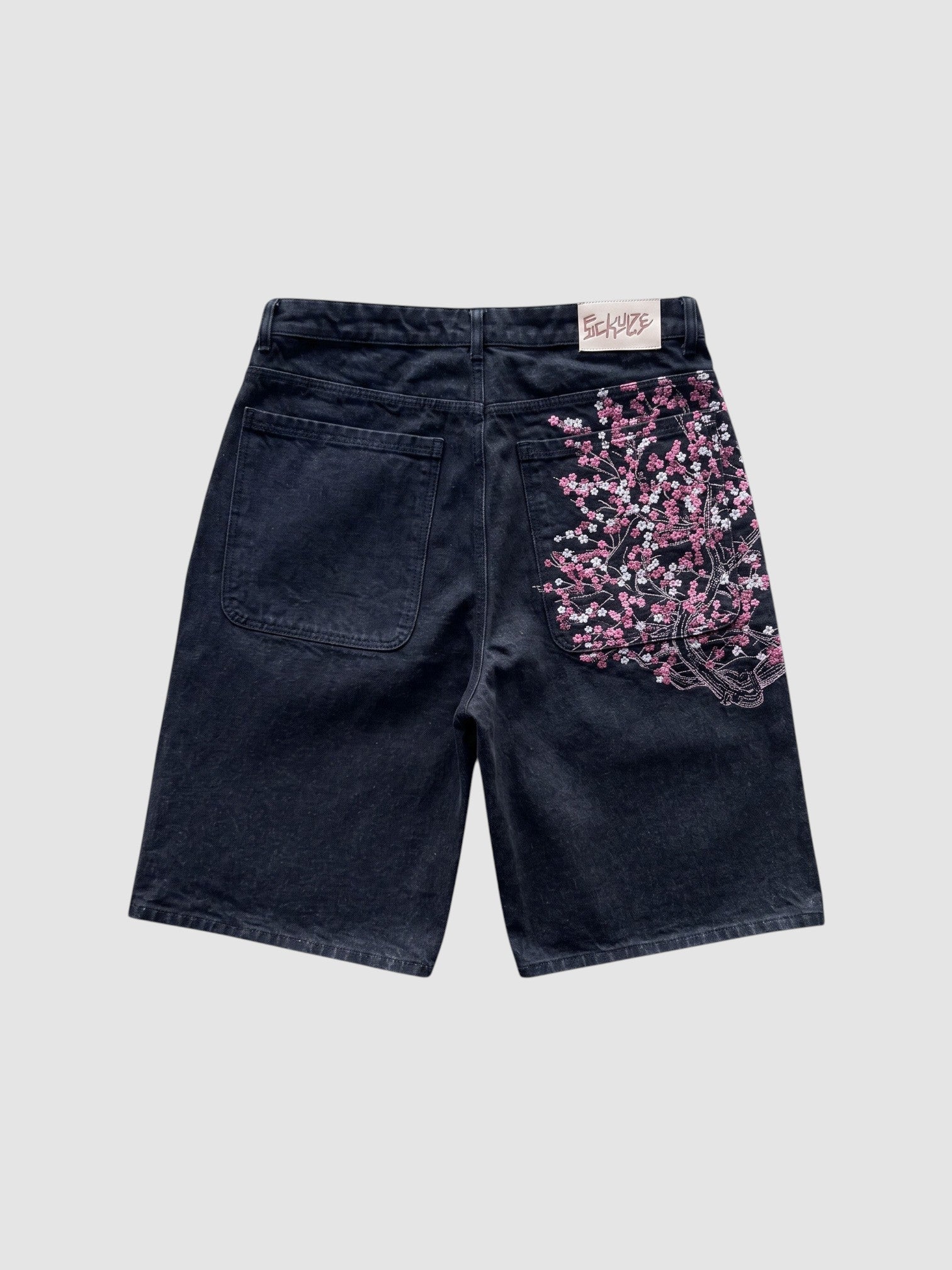 Y2K Studio black denim jorts featuring intricate pink and white cherry blossom embroidery on the back pocket.