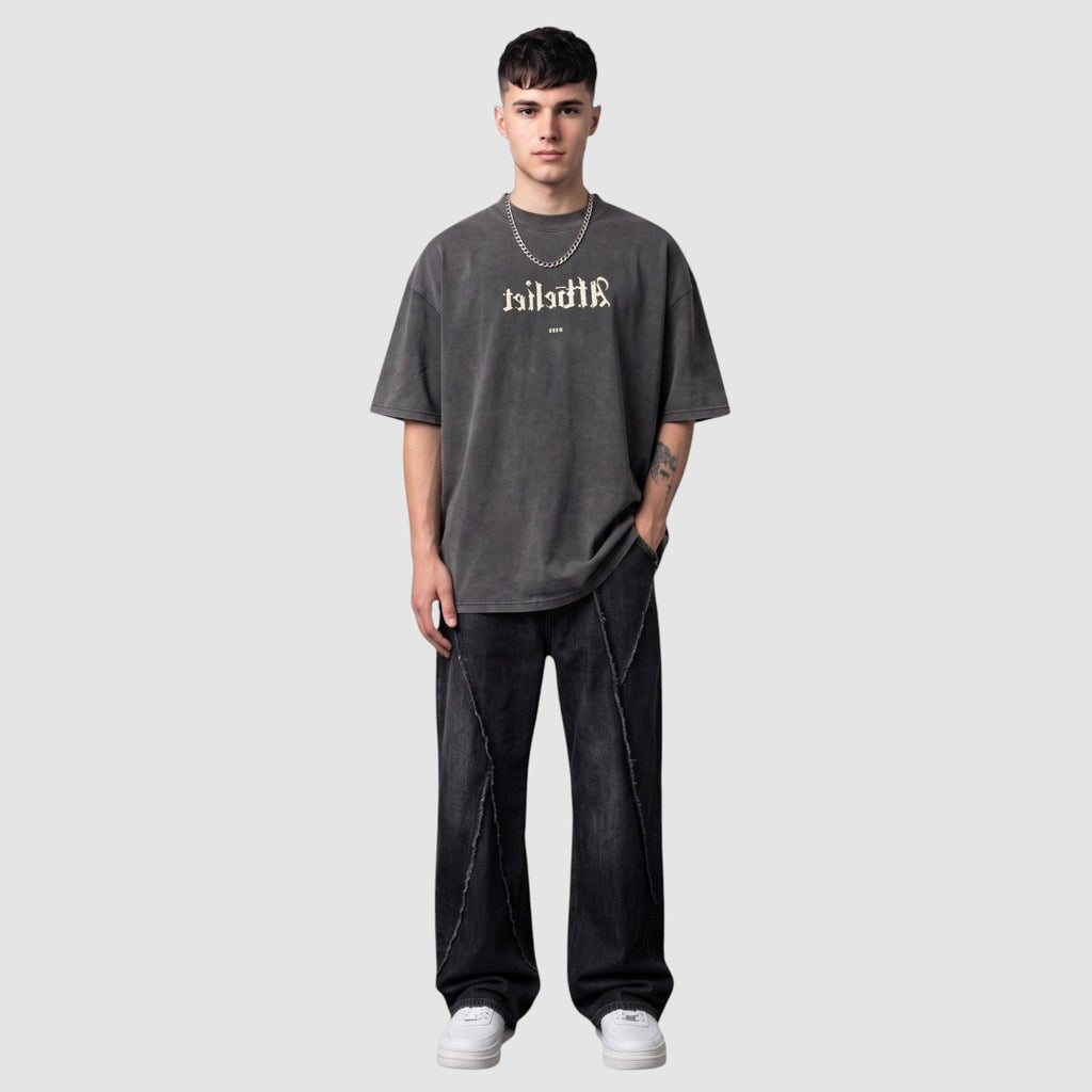 Y2K Studio black Y2K jeans with diagonal raw-edge seams worn by a model with a grey graphic t-shirt and sneakers