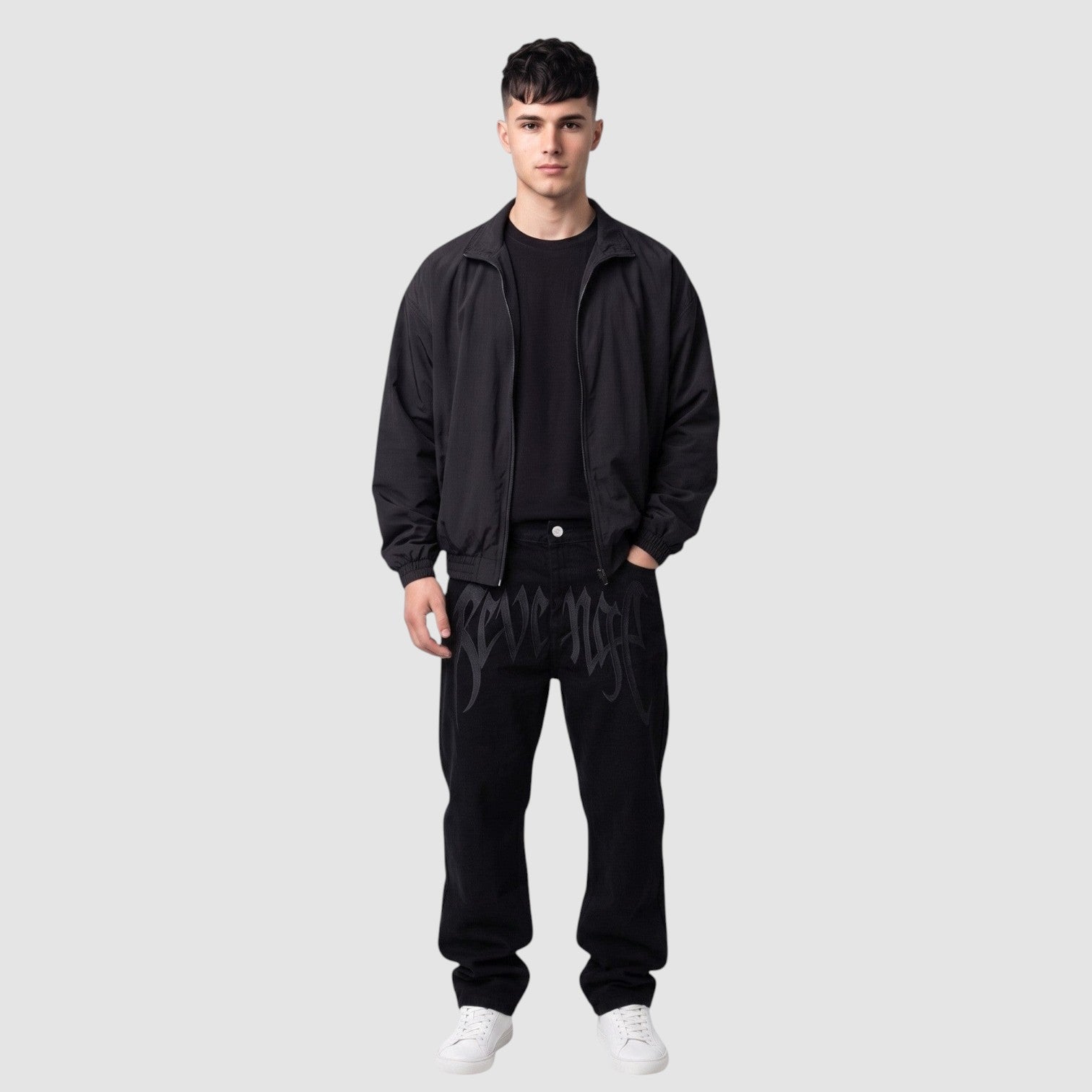 Y2K Studio black Y2K hip-hop jeans with gothic lettering on thighs, worn by a model with a black jacket and sneakers