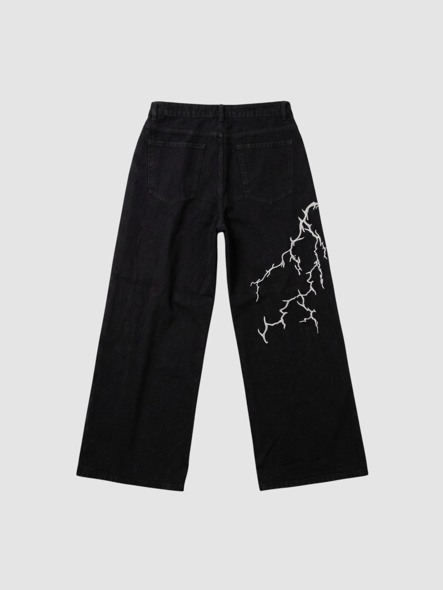 Y2K Studio black wide-leg denim jeans featuring an asymmetrical white lightning bolt embroidery on the back leg.