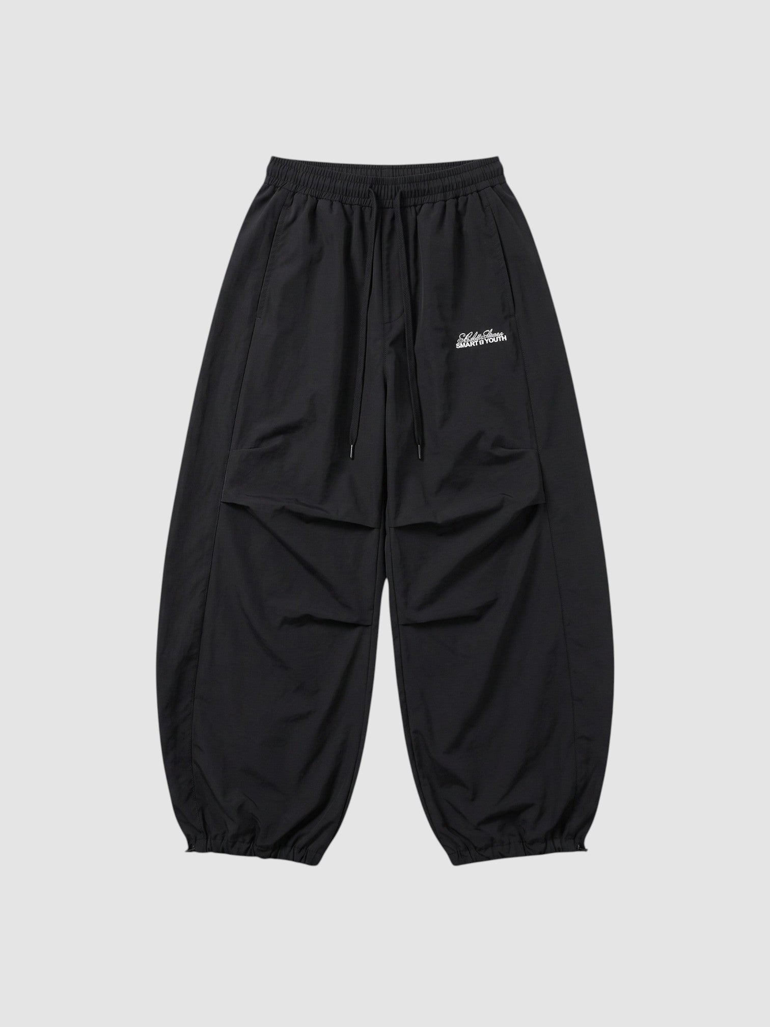 Y2K STUDIO black oversized nylon joggers with elastic waist, side pockets, and white script logo on the right thigh.