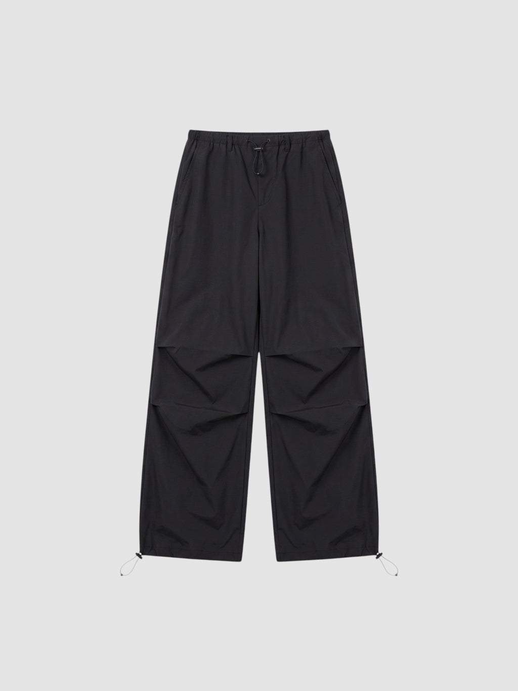 Y2K STUDIO black parachute pants with high elastic waist, adjustable drawstring cuffs, and pleated knee detailing.