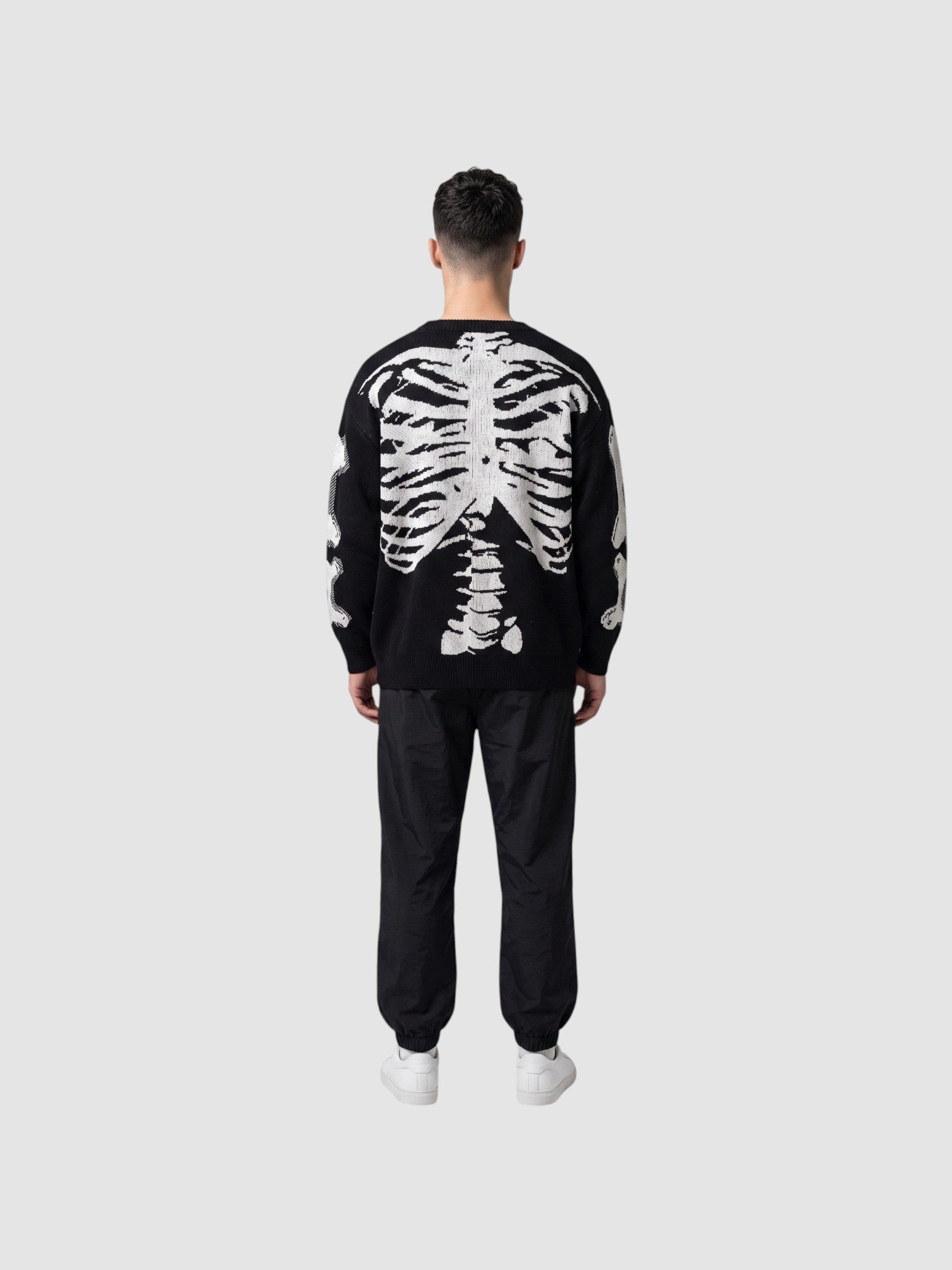 Y2K STUDIO black knit sweater with white 3D skeleton ribcage and spine design on the back, worn by a man.