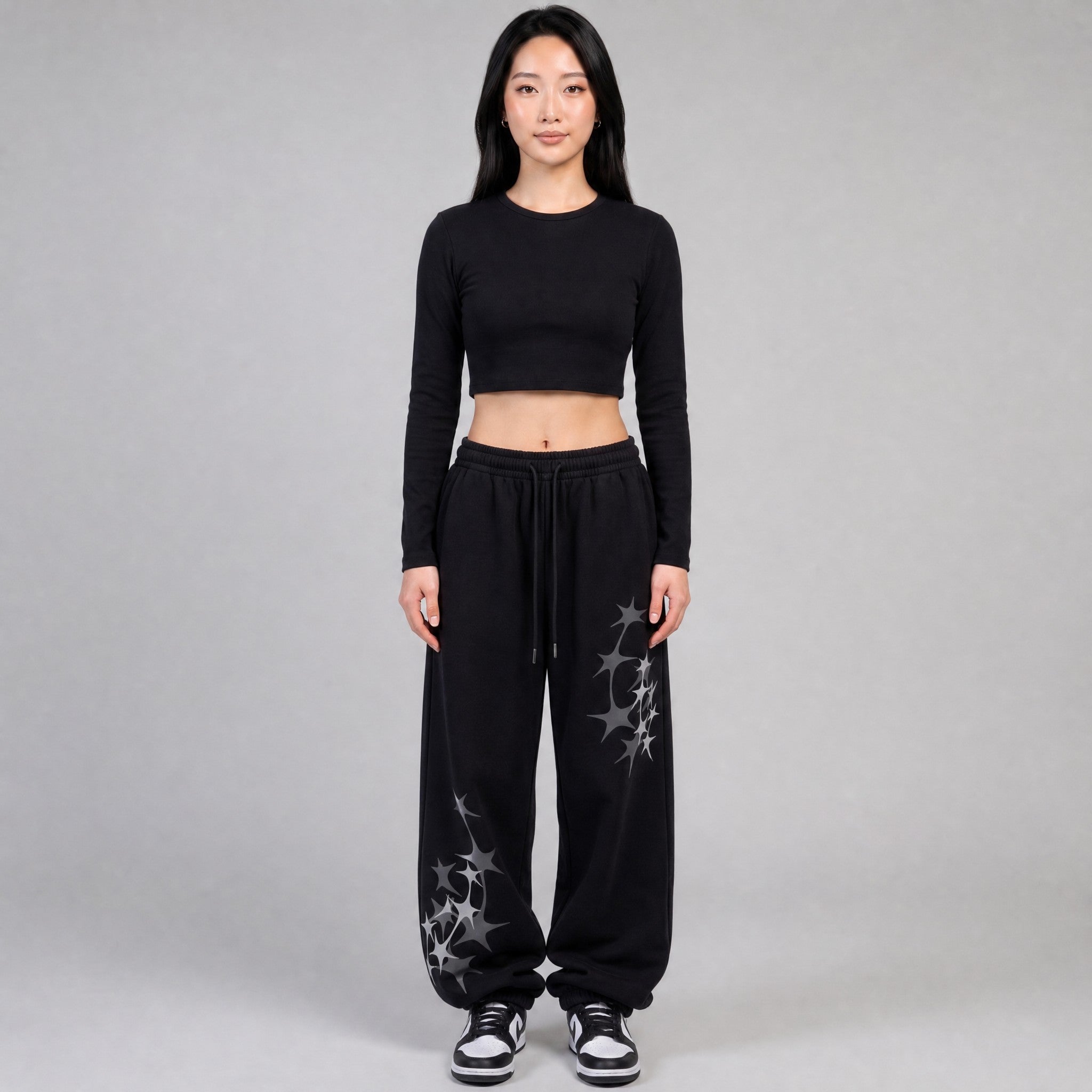 Y2K STUDIO black wide leg joggers with grey star prints, elastic waist, and white drawstring on a female model
