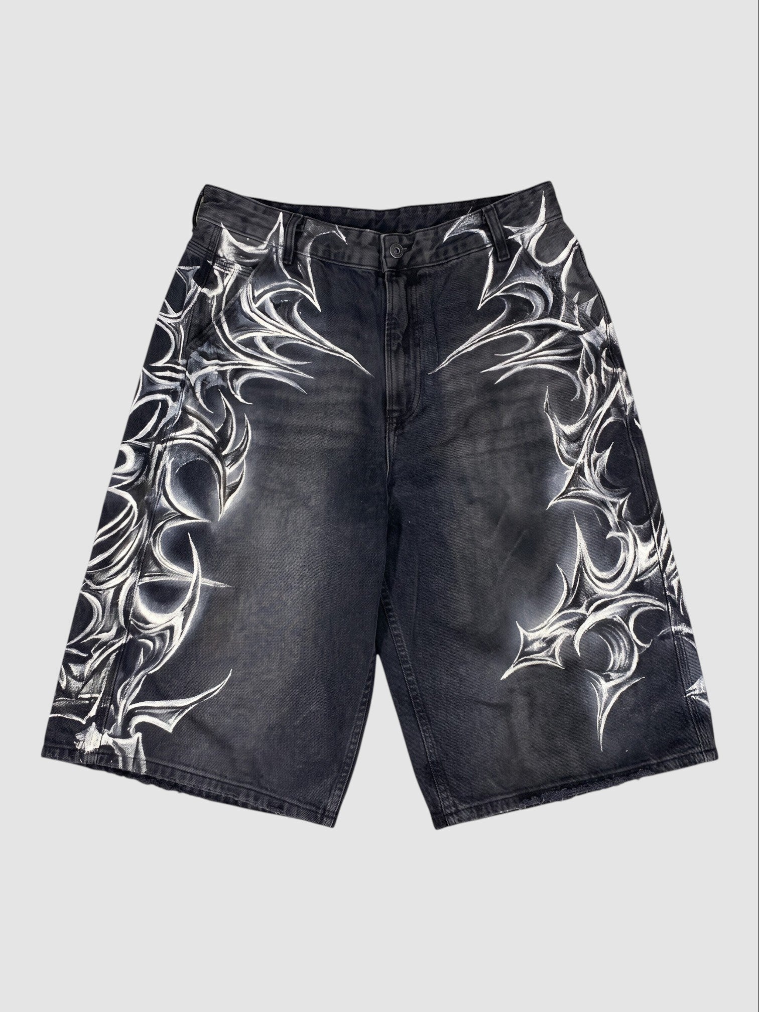 Y2K Studio black denim jorts featuring white airbrushed tribal motifs and a loose, knee-length fit with raw hems.