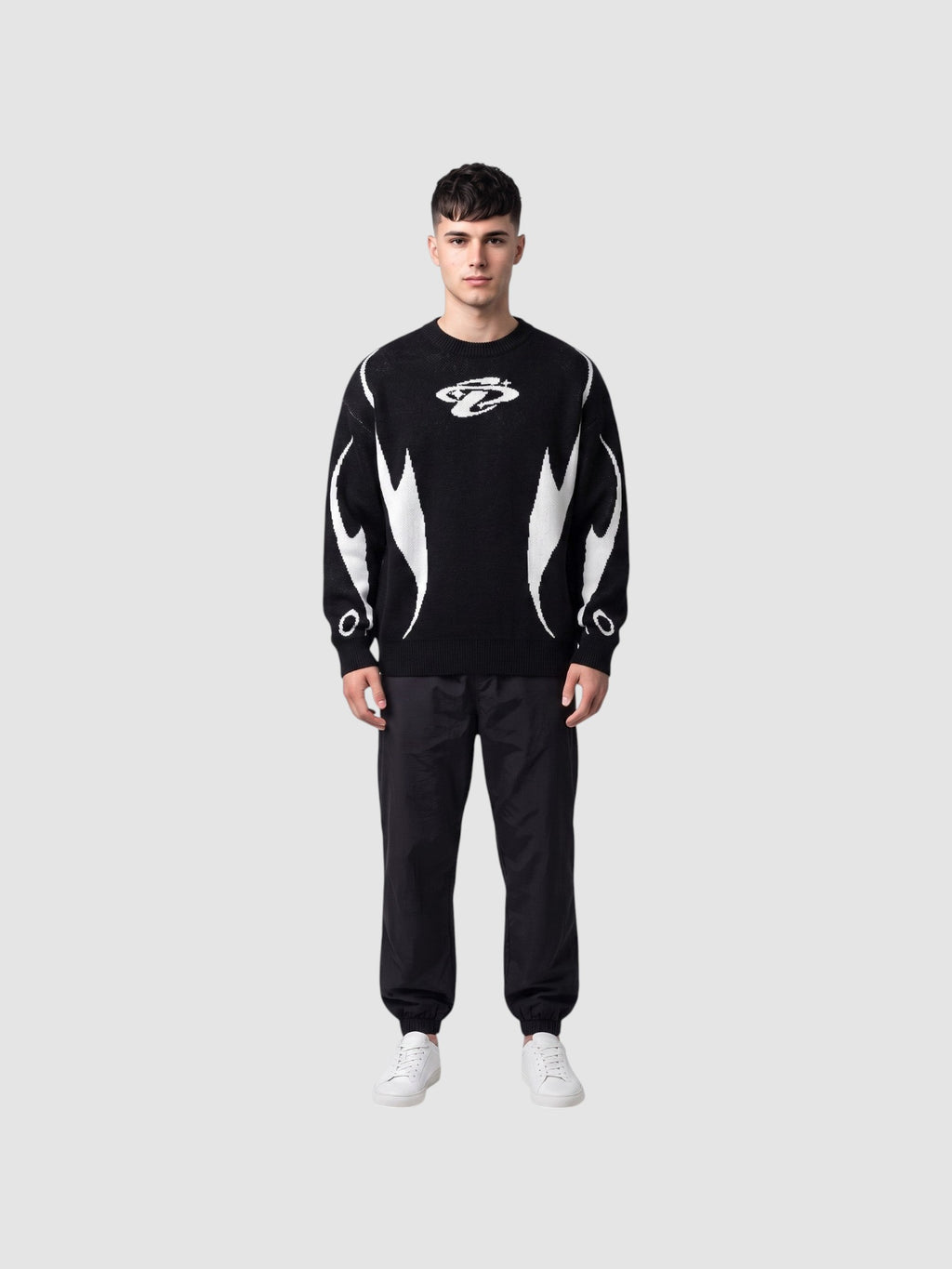 Y2K STUDIO black and white knit sweater with flame motifs and chest logo worn by a male model with black trousers