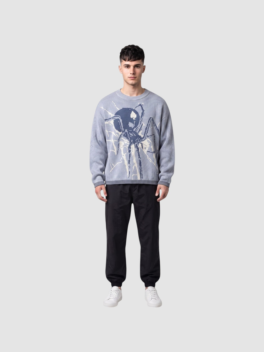 Y2K STUDIO blue knit sweater featuring a large spider web graphic, worn by a man with black trousers and sneakers.