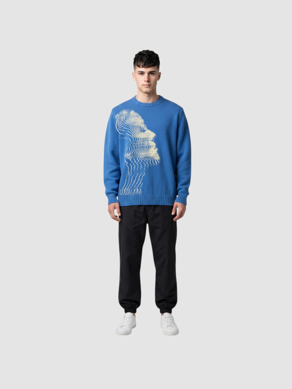 Model wearing Y2K STUDIO blue oversized knit sweater with cream wavy face graphic, paired with black cargo pants