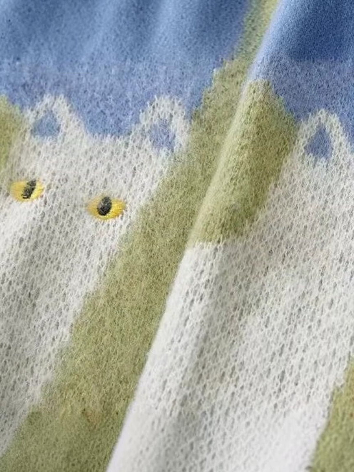 Close-up of Y2K STUDIO knit sweater featuring a cat pattern with yellow eyes on a blue and green gradient background