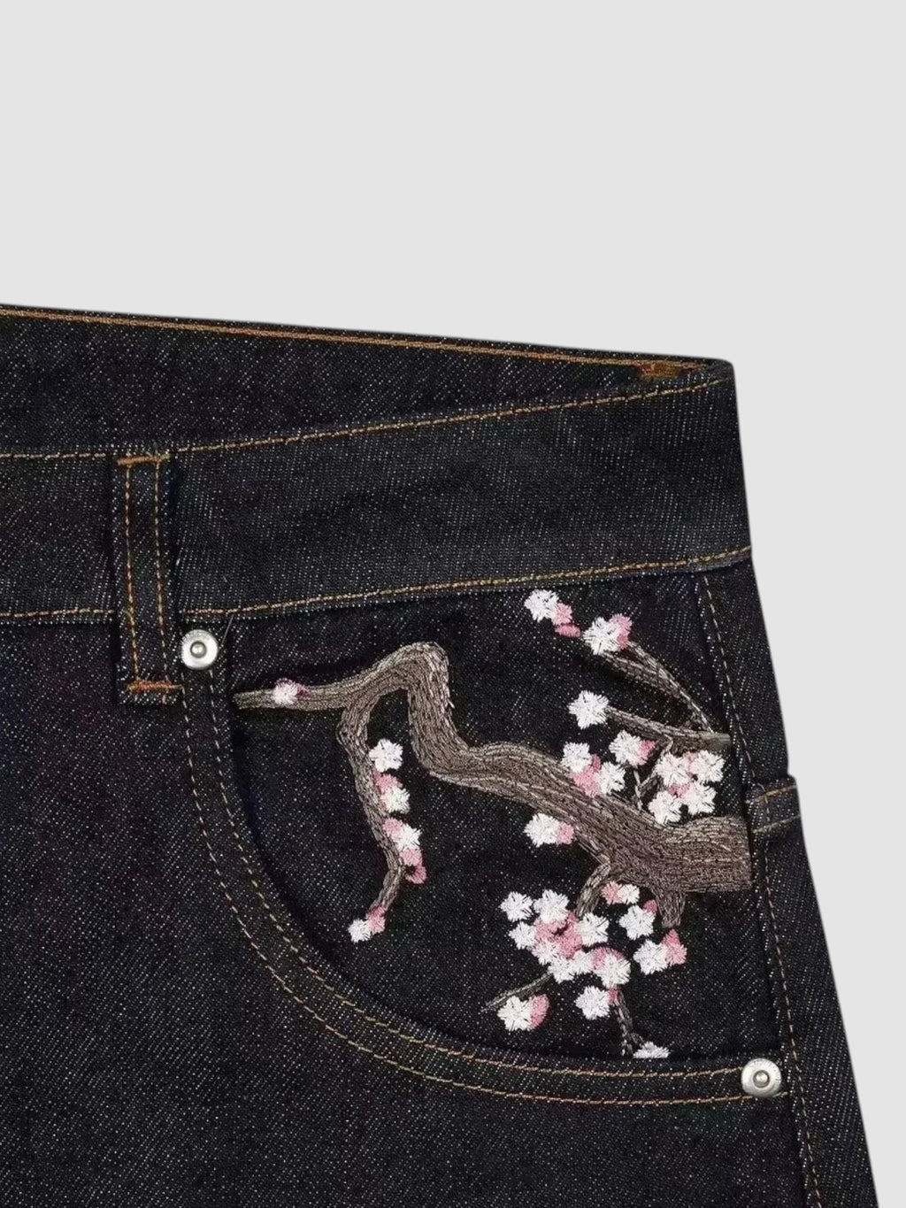 Y2K Studio dark denim jeans featuring detailed cherry blossom embroidery on the back pocket in pink and white thread.