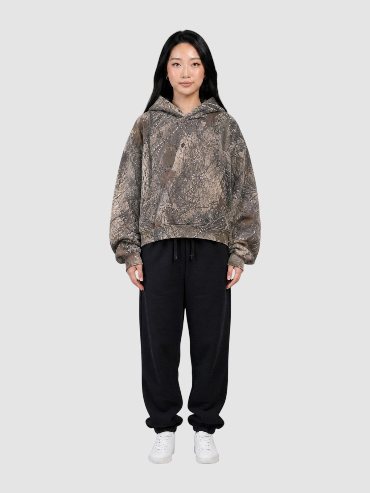 Model wearing Y2K Studio cropped camouflage hoodie with tree bark print and boxy fit paired with black sweatpants