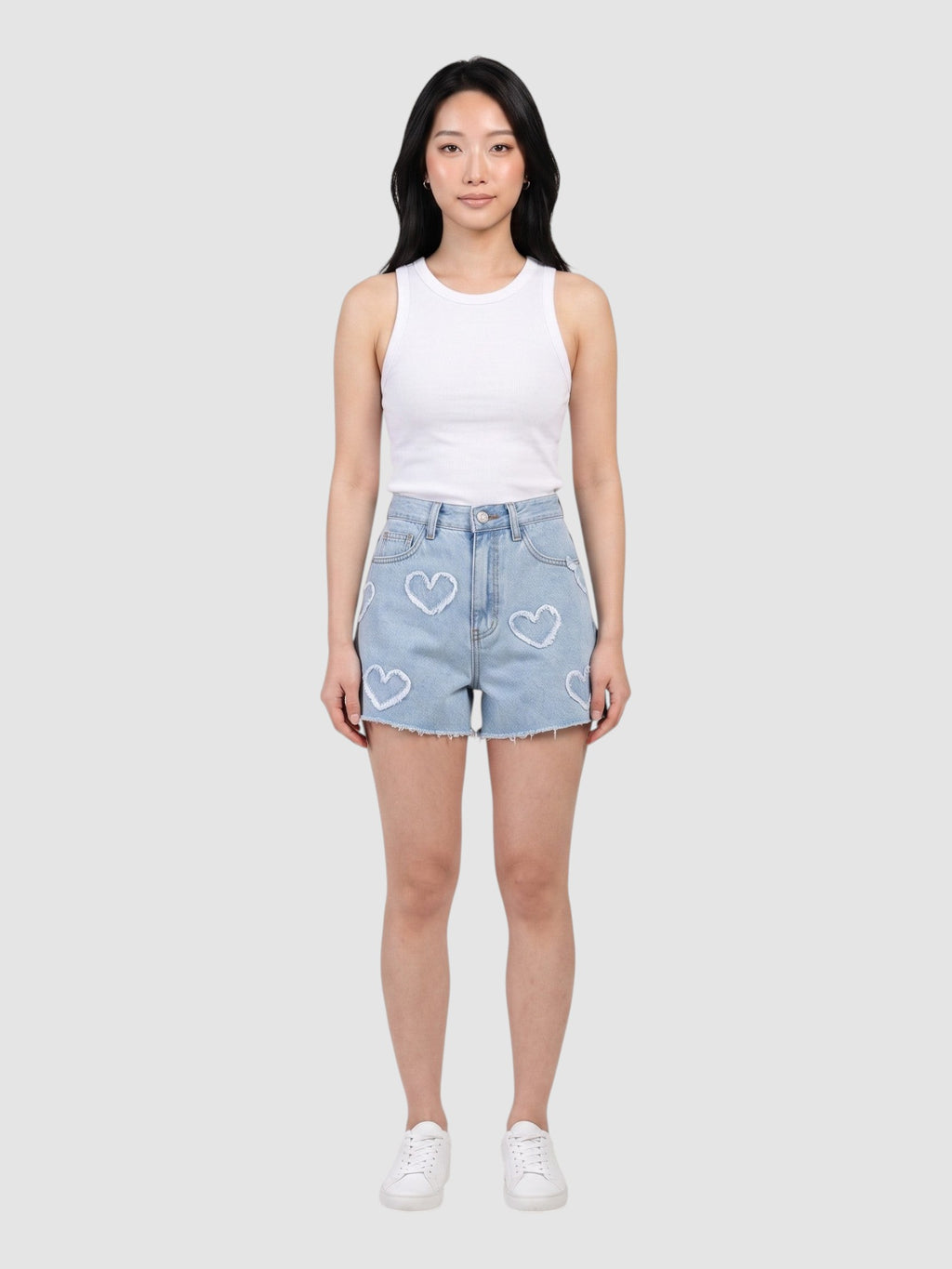Model wearing Y2K STUDIO light blue high-waisted denim shorts with frayed heart applique details and raw hem.