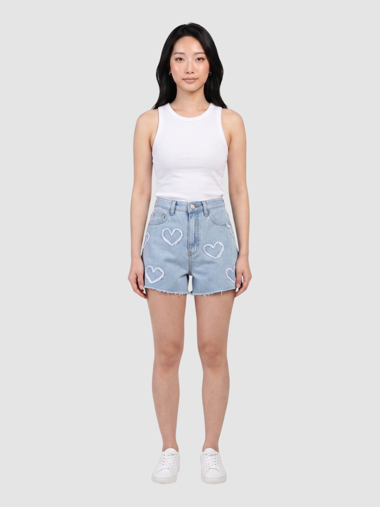Model wearing Y2K STUDIO light blue high-waisted denim shorts with frayed heart applique details and raw hem.