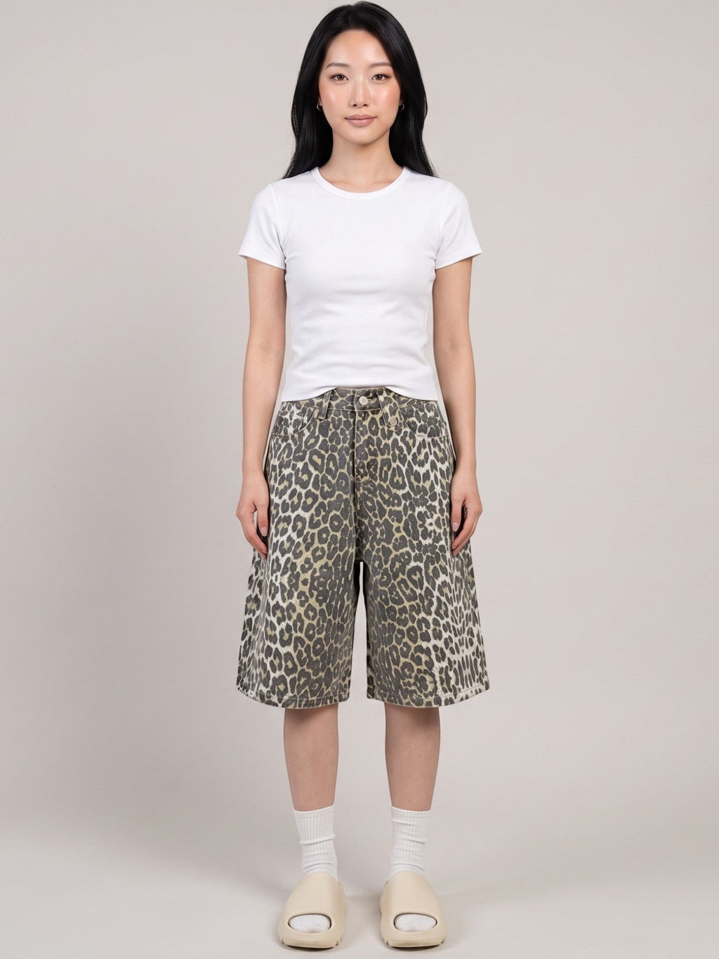Model wearing Y2K Studio high-waisted khaki leopard print denim bermuda shorts with a white t-shirt and slides.