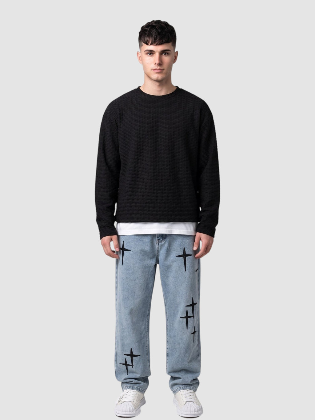 Y2K Studio light wash denim jeans with black embroidered cross motifs worn by a man with a black textured sweater