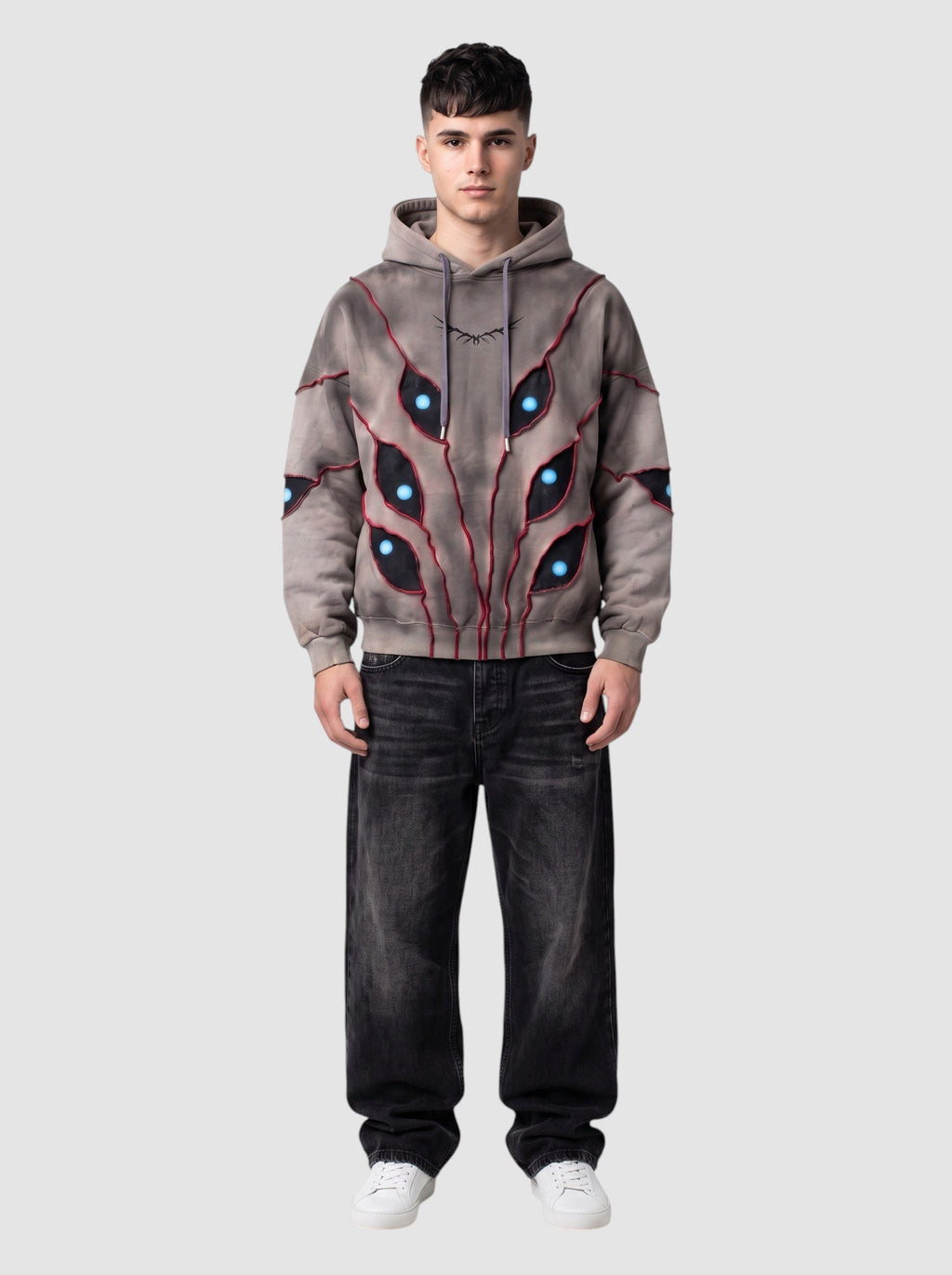 Y2K Studio oversized beige hoodie with patchwork eye cutouts, blue pupils, and red stitching on a male model
