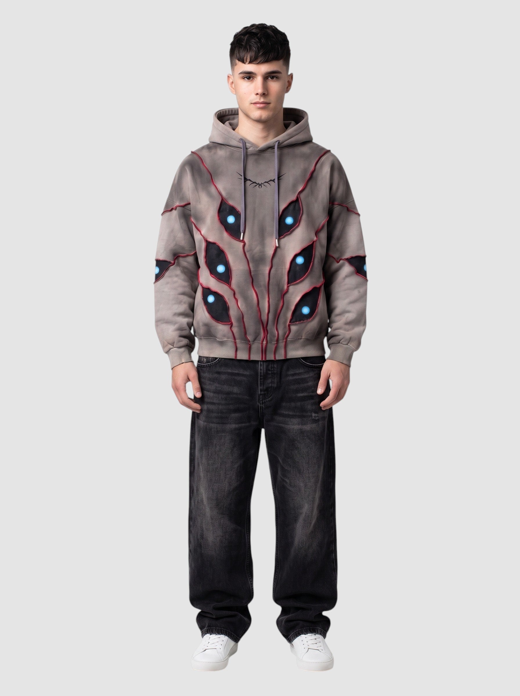 Y2K Studio oversized beige hoodie with patchwork eye cutouts, blue pupils, and red stitching on a male model