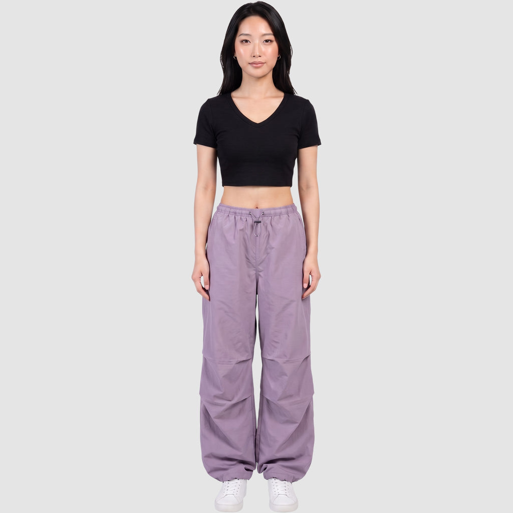 Model wearing Y2K STUDIO high-waisted purple parachute pants in matte nylon with drawstring waist and ankles.