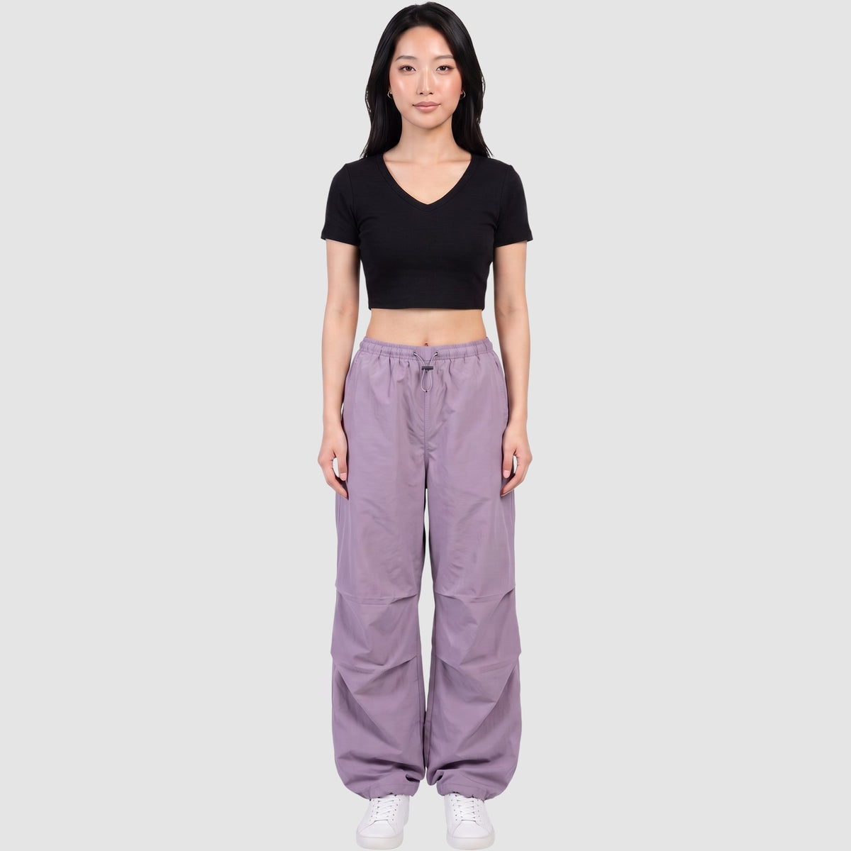 Model wearing Y2K STUDIO high-waisted purple parachute pants in matte nylon with drawstring waist and ankles.