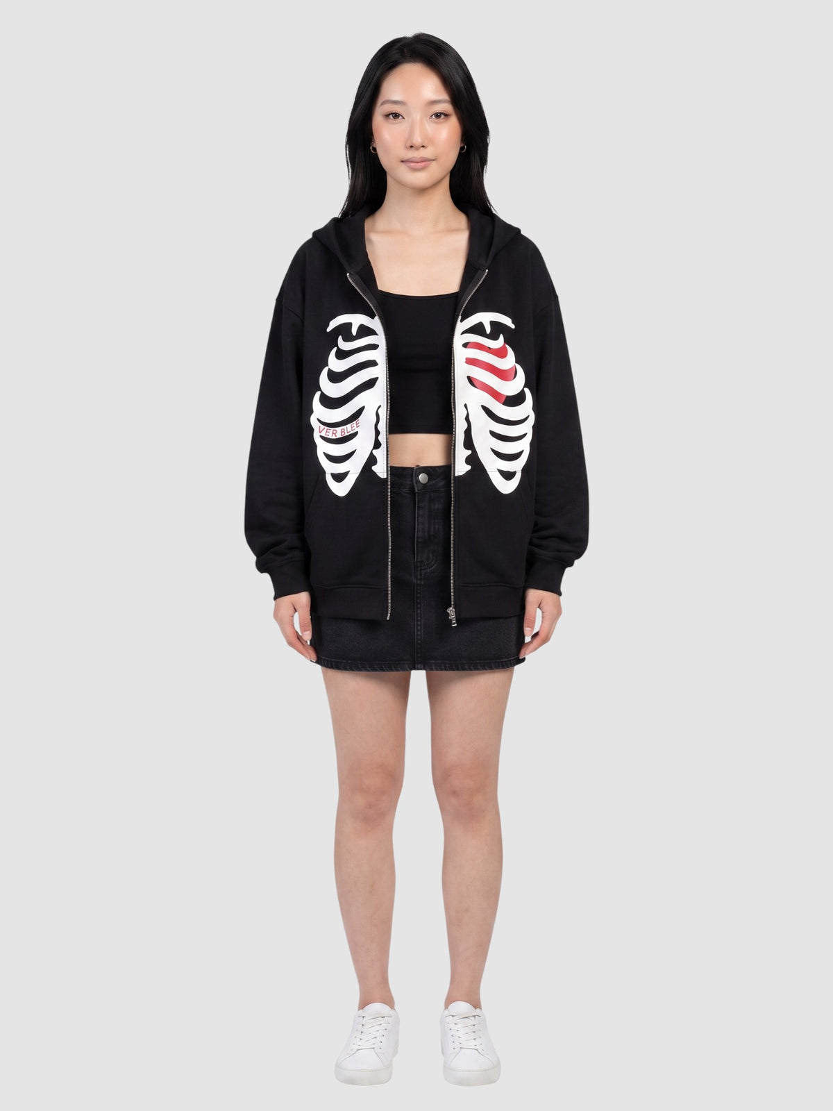 Model wearing a Y2K Studio black zip-up hoodie featuring a white skeleton rib cage print and a red heart detail.