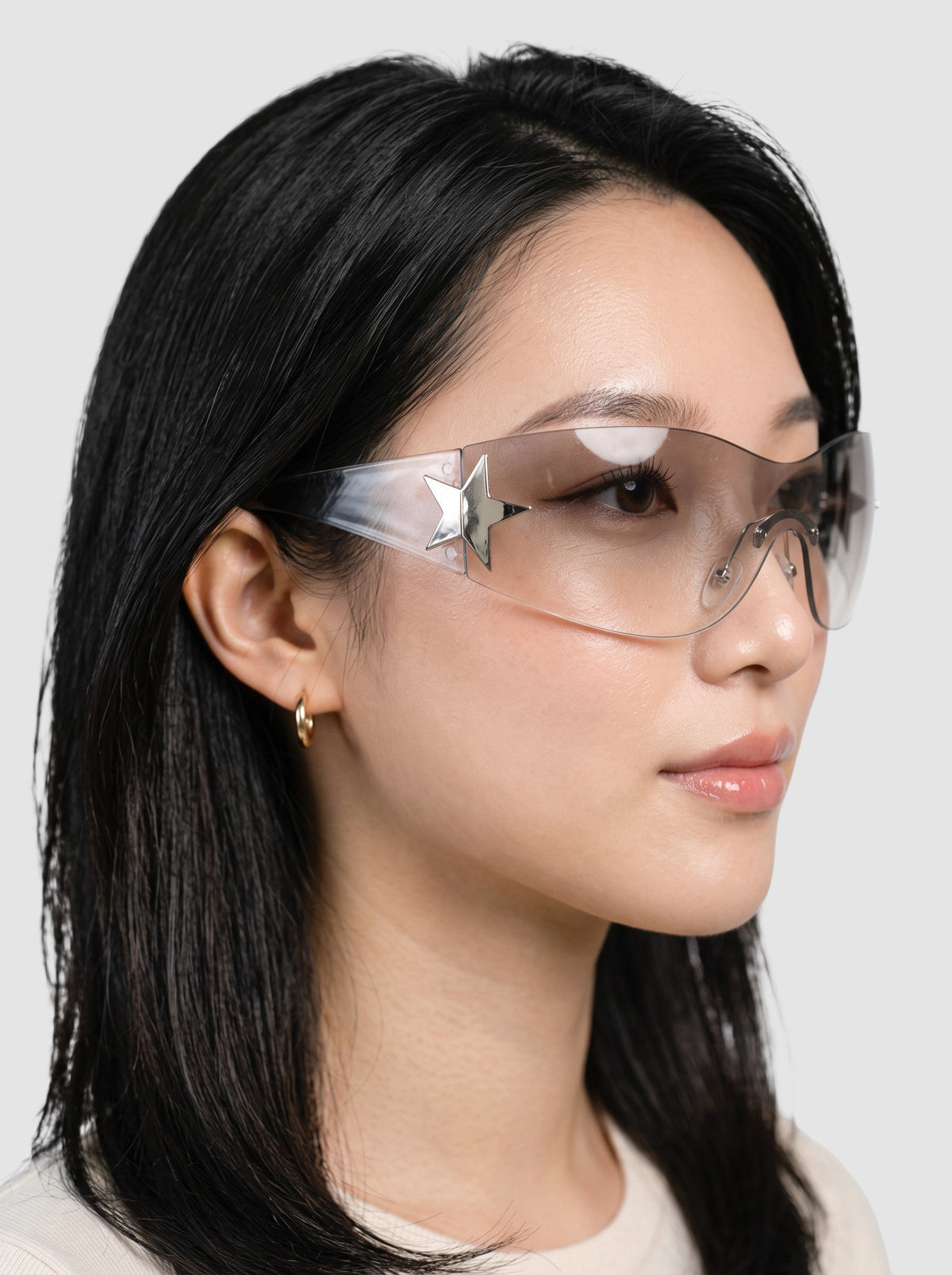 Y2K Studio Y2K star mask sunglasses with a frameless clear shield lens and silver star detail worn by a model