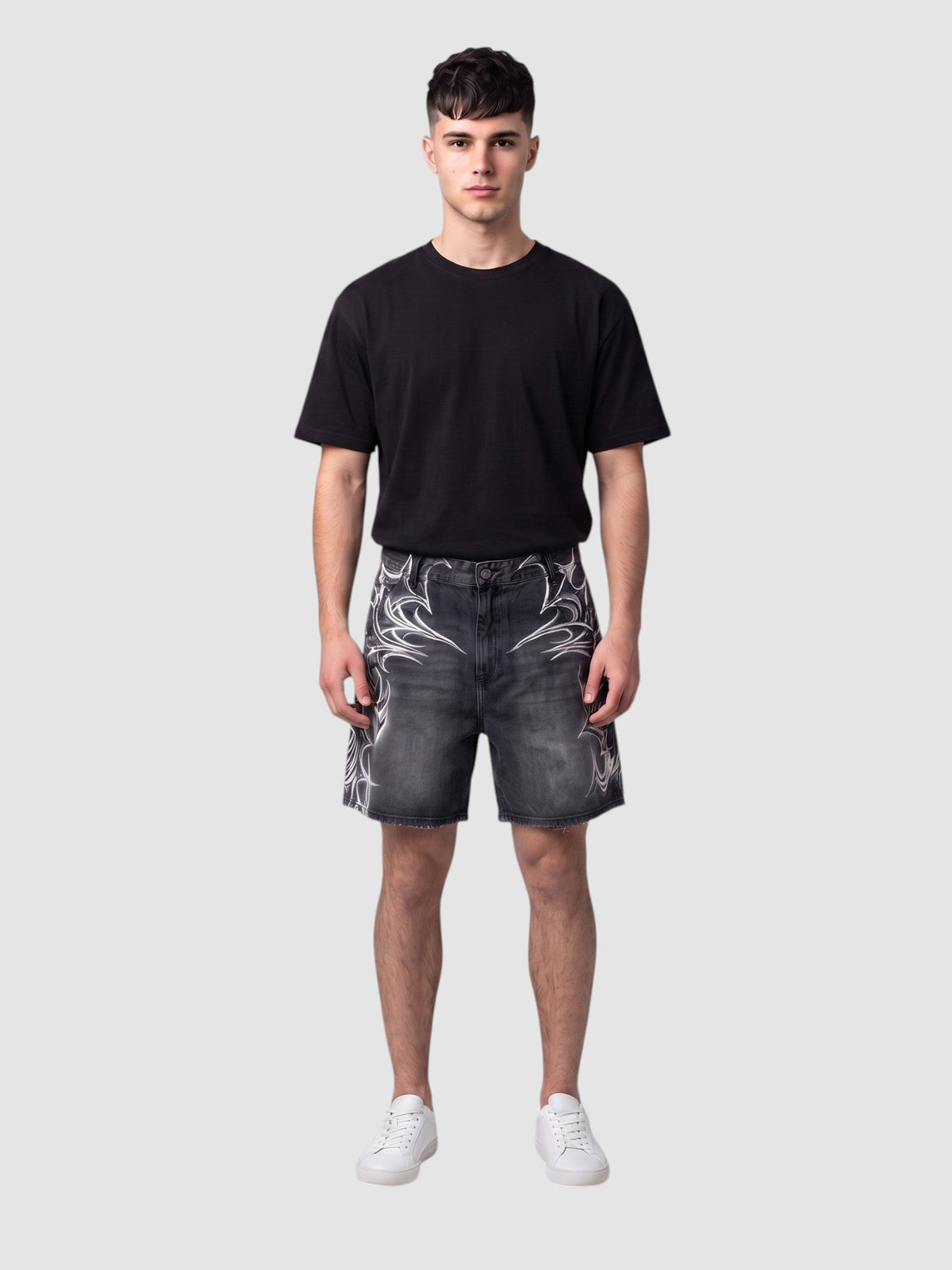 Y2K Studio black denim jorts featuring white airbrushed tribal motifs, raw hem, and loose fit on a male model.