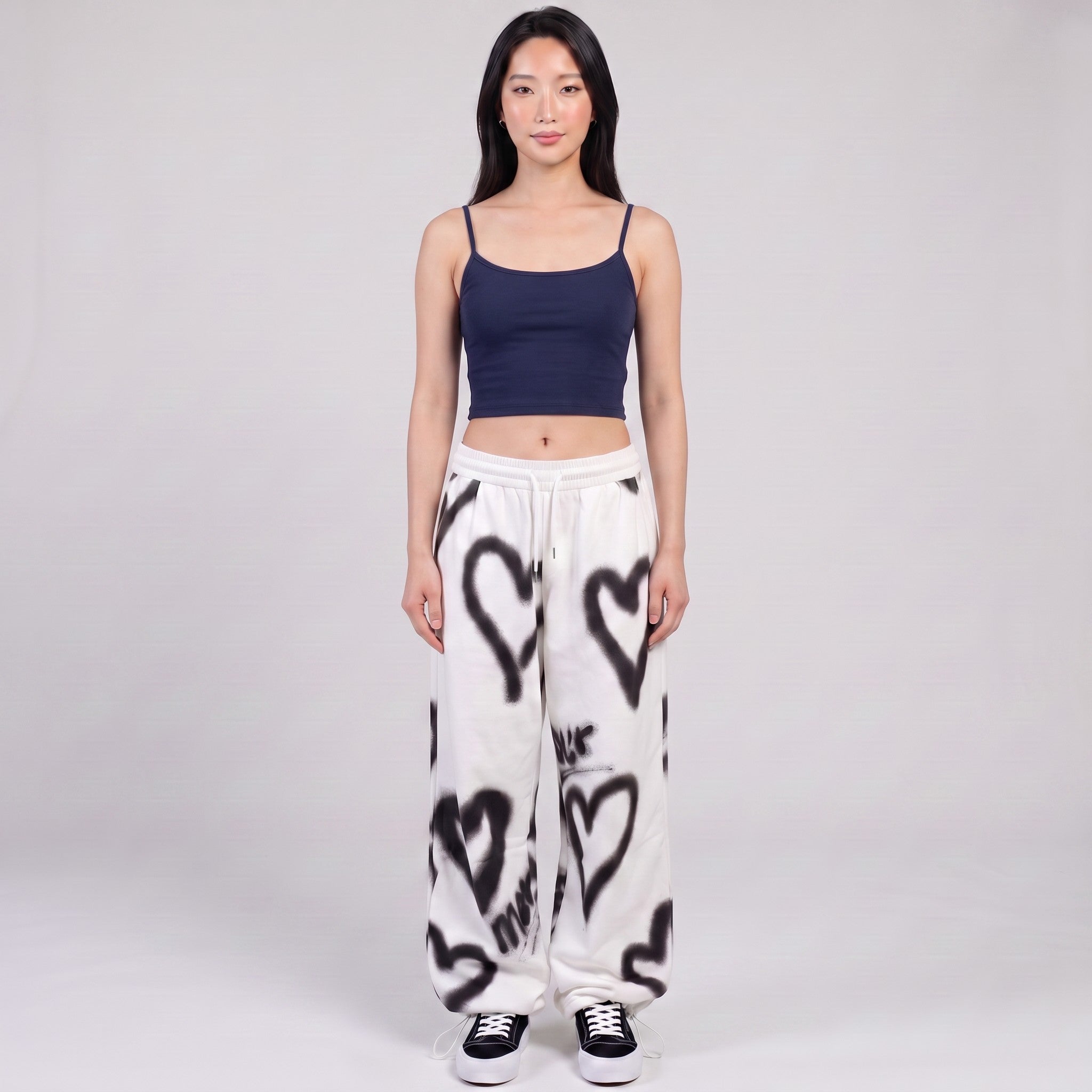 Y2K STUDIO white wide-leg sweatpants with black spray-painted heart motifs, worn with a navy crop top by a model.
