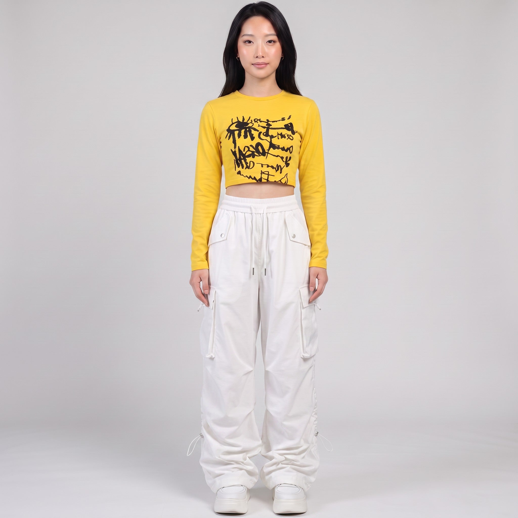 Model wearing Y2K STUDIO white high-waisted parachute cargo pants with side pockets and a yellow cropped long-sleeve top